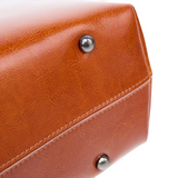 A close-up view of a brown leather bag with a metal button on the top.