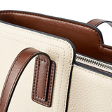 A close-up view of a beige leather handbag with brown leather accents, including a zipper and handle.