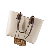 A tan leather handbag with brown leather straps is displayed on a wooden block against a white background.