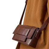 A brown leather handbag with a structured design and a strap.