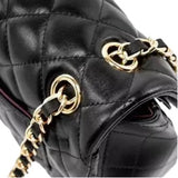A close-up view of a black leather handbag with gold-colored metal hardware, including two round buckles and a chain strap.