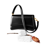 A black leather handbag with a gold metal clasp and strap is displayed against a white background.