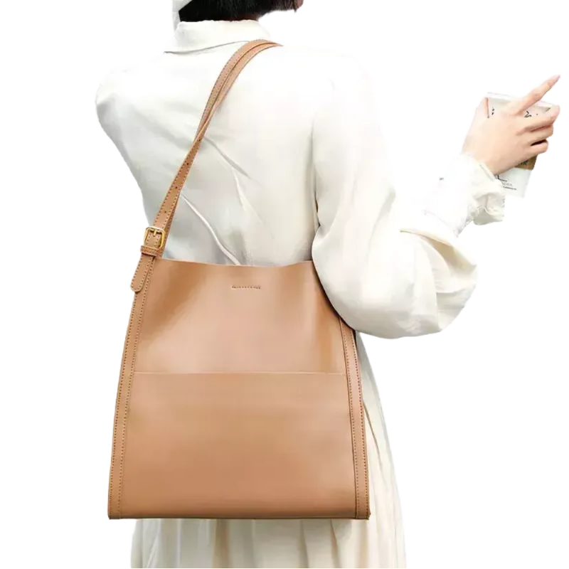 A woman wearing a white dress and carrying a tan leather shoulder bag is shown in the image.
