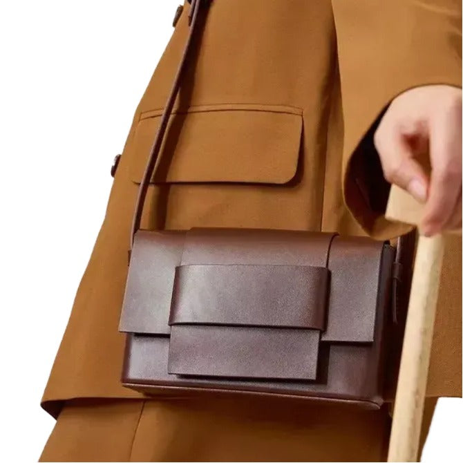 A close-up of a person wearing a brown jacket and carrying a brown leather handbag.