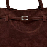 A close-up view of a brown suede handbag with a metal buckle detail.