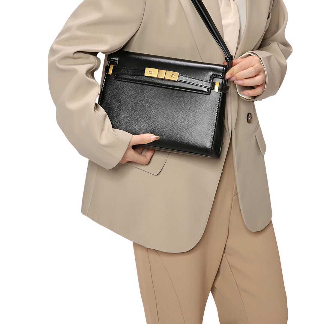 A person wearing a beige blazer and tan pants is holding a black leather handbag with gold hardware.