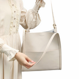 A person wearing a white dress is holding a large white handbag.