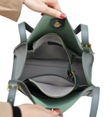 A person's hand holding a green leather handbag with a zipper and a gold buckle.