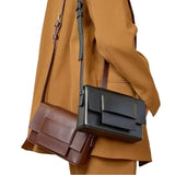 A person wearing a brown coat and carrying a black and brown handbag.