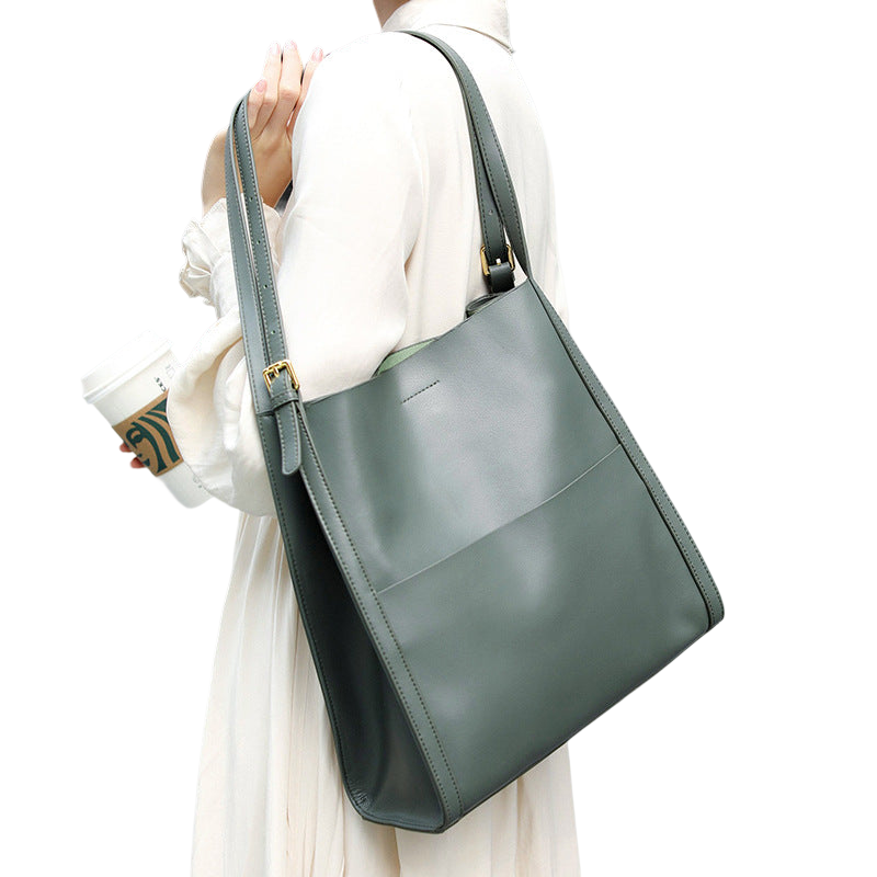 A person wearing a white dress is holding a large green tote bag and a coffee cup.
