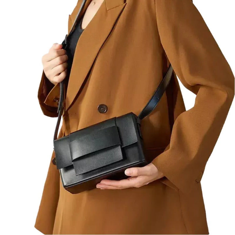 A person wearing a brown coat is holding a black handbag.