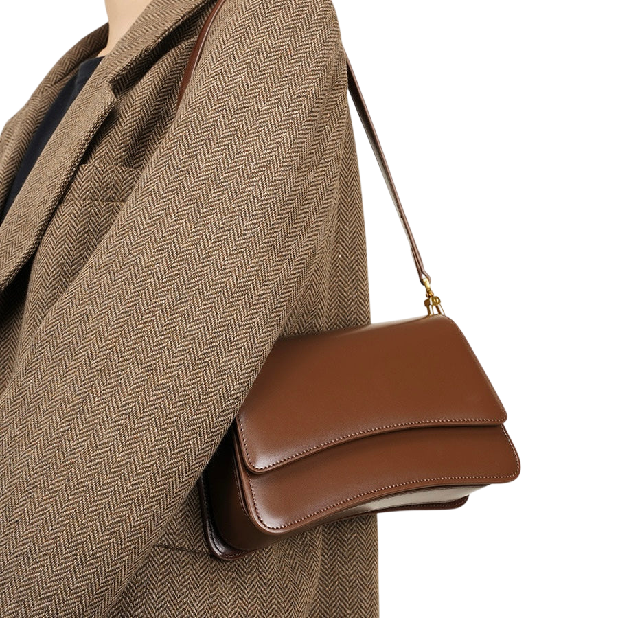 A brown leather handbag is being carried by a person wearing a brown tweed jacket.