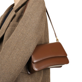 A brown leather handbag is being carried by a person wearing a brown tweed jacket.