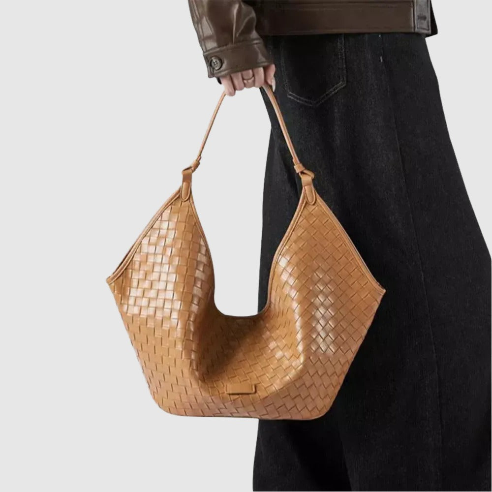 A person is holding a tan woven handbag with a distinctive shape and pattern.
