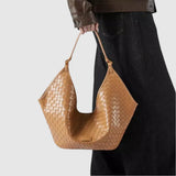 A person is holding a tan woven handbag with a distinctive shape and pattern.