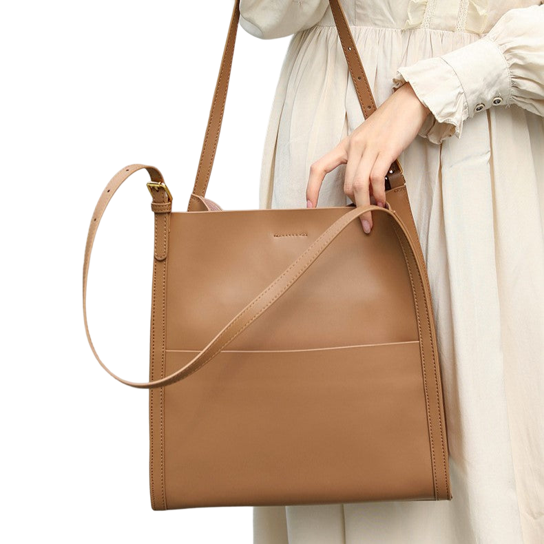 A woman wearing a white dress is holding a tan leather handbag with a strap.