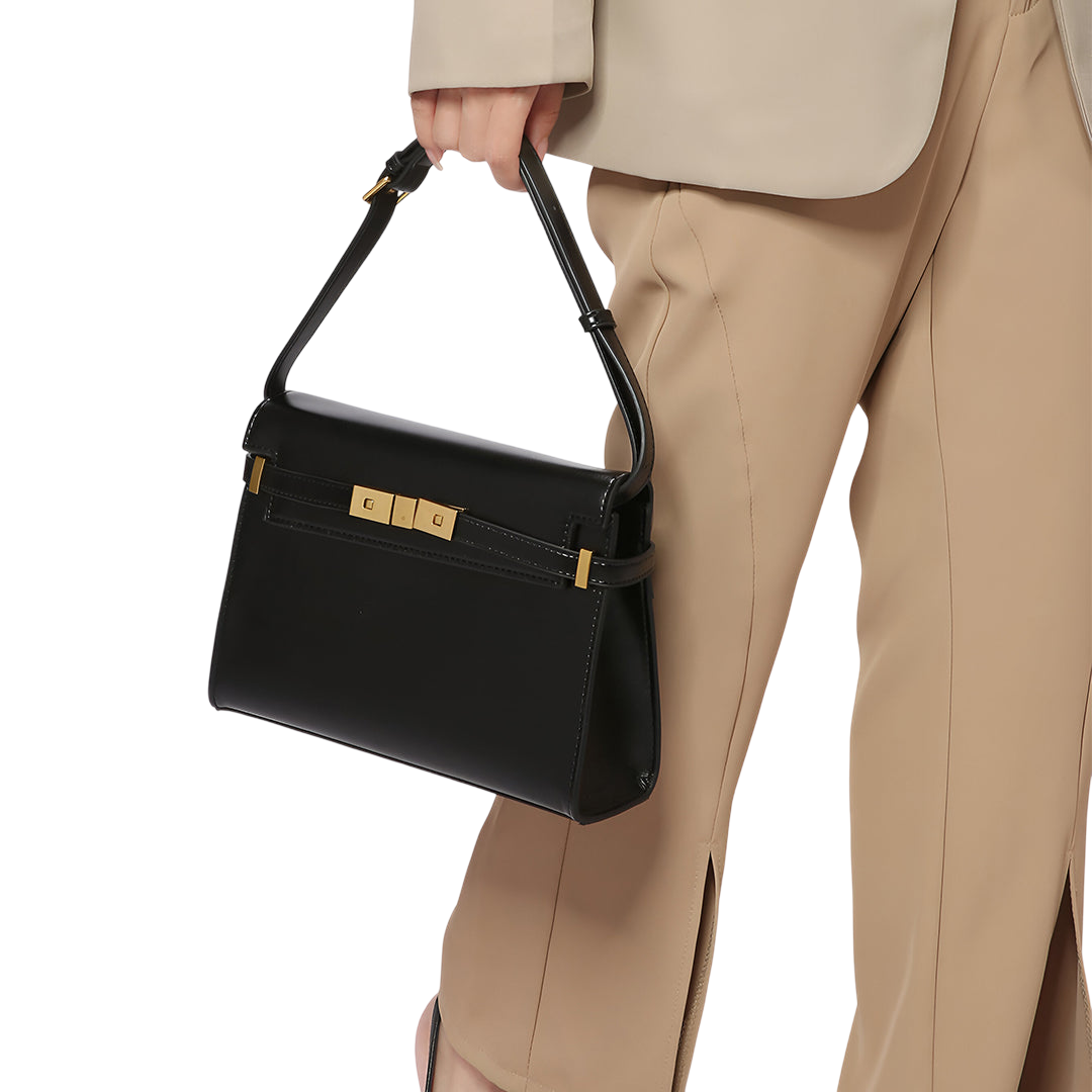 A person is holding a black handbag with gold hardware.