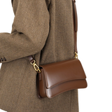 A brown leather handbag with a gold metal clasp and strap is being worn by a person.