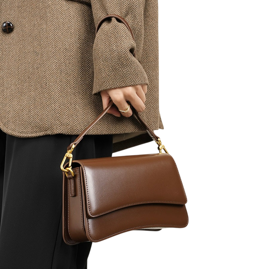 A person wearing a brown tweed jacket and holding a brown leather handbag.