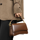 A person wearing a brown tweed jacket and holding a brown leather handbag.