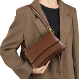 A person wearing a brown tweed jacket and carrying a brown leather handbag.